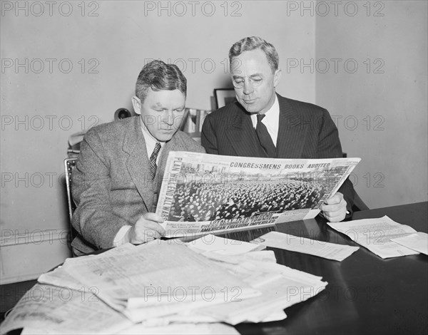 Two men sitting at a desk reading a newspaper