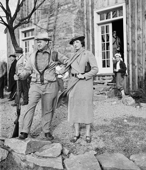 Well dressed woman with man holding rifle or shotgun