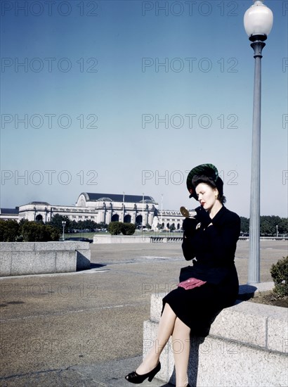 Woman putting on her lipstick in a park with Union Station behind her