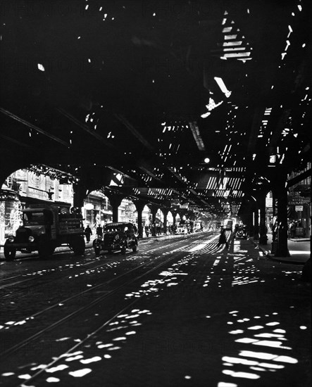 1930s New York City - Patterns of light illuminate darkness under elevated railroad tracks, pedestrians, car, truck visible ca. 1936