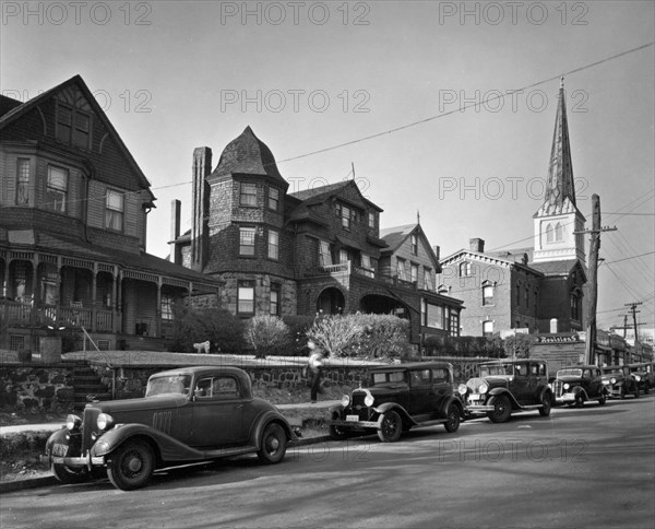 Looking up street, Queen Anne house at left, church, businesses at right, Shingle style and another house in middle, cars along the street. St. Mark's Place, no. 340-348, Staten Island ca. 1937