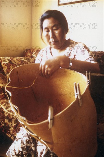 Eskimo woman from the village of Ambler Alaska making traditional birch bark basket for harvesting of berries ca. 1975