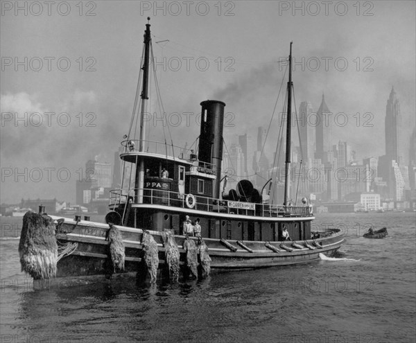 Looking broadside at the tugboat Watuppa, with the lower Manhattan (from the Municipal Bldg. south) skyline in the background ca. 1936
