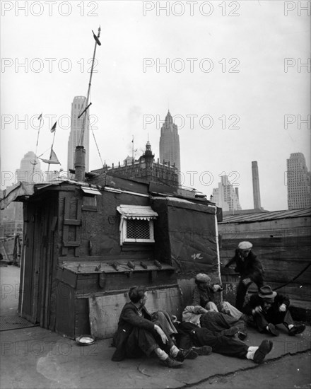 Men in front of shelter, decorated with flags on masts, ship-carvings, window with awning. One man seems to have just hit another ca. 1938