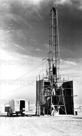Dr. Robert Goddard's 22 foot rocket in it's launching tower, 1940, near Roswell, New Mexico. N.T. Ljungquist on the ground, A.W. Kisk working on rocket and C. Mansur at top of tower.