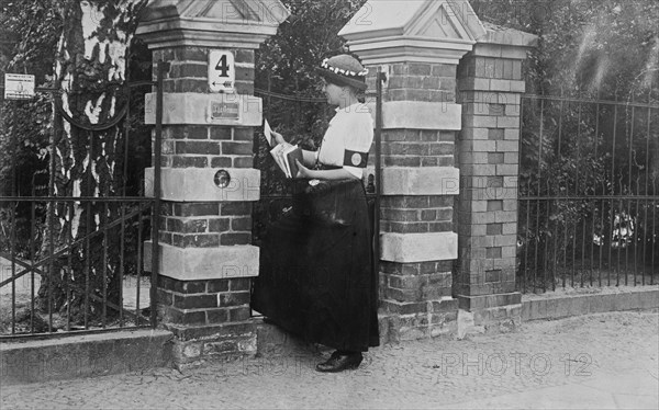Woman mail carrier at a gate of a house, in Berlin, Germany during World War I ca. 1910-1915