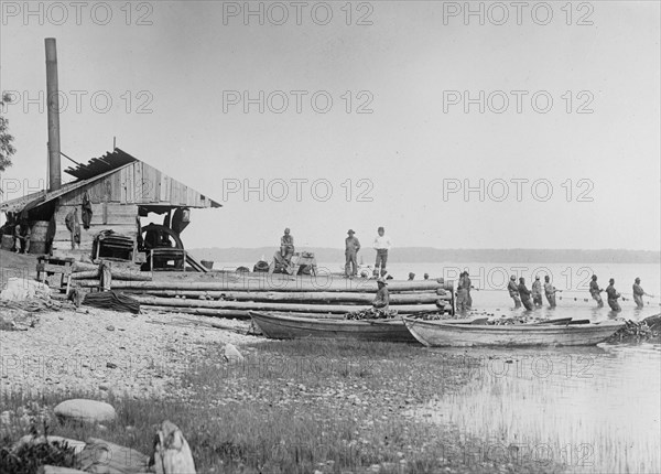 African American fishermen with net, standing in water near building ca. 1910-1915