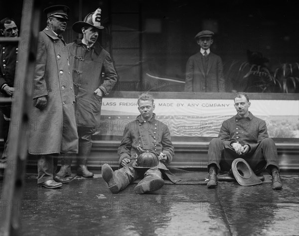 Firemen seated on the sidewalk after fighting a fire in a New York City subway tunnel which took place near West 55th Street and Broadway, January 6, 1915