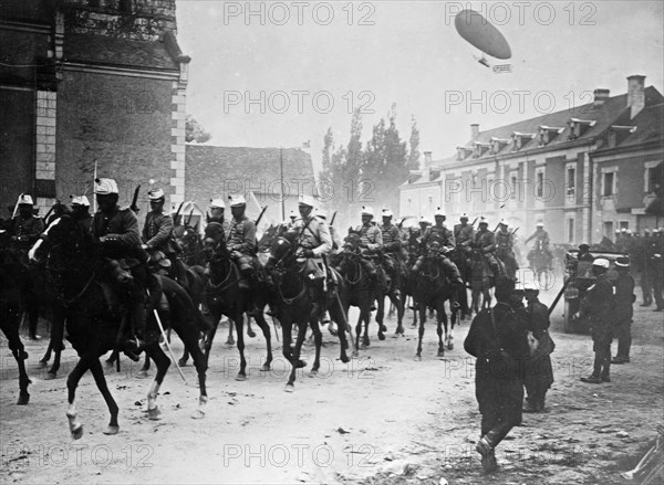 French soldiers on horseback in street, with airship Dupuy de Lome flying in air behind them during World War I ca. 1914-1915