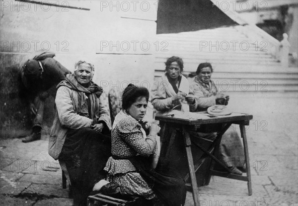 Older man and women sitting at a table in Amalfi Italy, possibly at the bottom of the steps leading to the Amalfi Duomo ca. 1910-1915