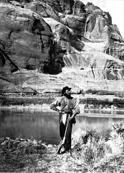 John F. Steward, a member of the Powell Survey, in Glen Canyon, Colorado River. He is shown with the typical field equipment of those early Surveys: gun, pick, map case, and a canteen. This photo was taken in Kane County, Utah in 1872.