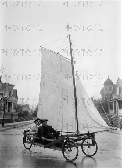 Two young adults having fun riding in a sail wagon or sail cart riding down a street in Brooklyn, possibly Victorian Flatbush ca. 1912