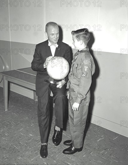 Mercury astronaut John Glenn holding a globe while talking with young boy, a boy scout or cub scout.