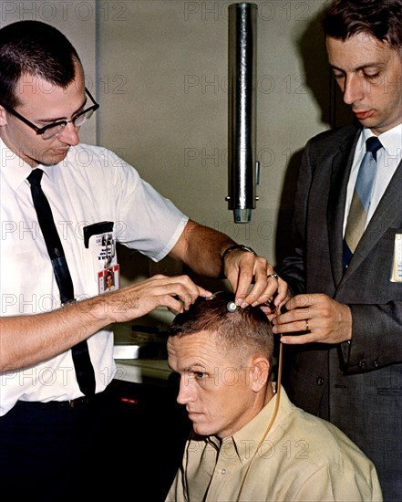 (2 Dec. 1965) Astronaut Frank Borman, Gemini-7 command pilot, sits attentively as two scalp electrodes are attached to his head.