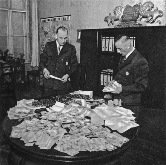 Preparation for shipment to Berlin of transport of gold coins and foreign currency stolen from Jews in Litzmannstadt Ghetto. Hans Biebow, first from the right ca. 1941-1943