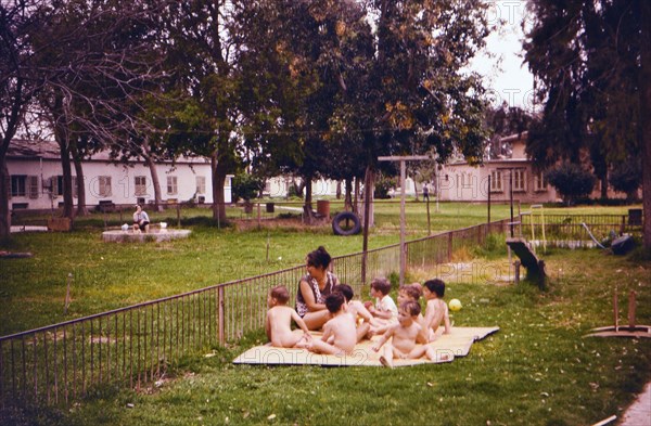 Israel April 1965:  Toddlers enjoying the fresh air, wearing no clothes, with a woman caretaker on an Israeli Kibbutz