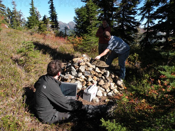 Pacific Northwest Seismic Network scientists checking data prior to uncovering an above ground seismic vault, Mount Baker, Washington ca. 2010