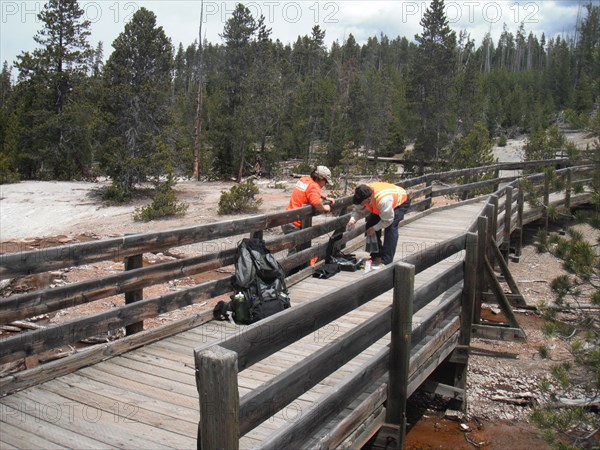 USGS scientists installing a temperature sensor under a public boardwalk in Norris Geyser Basin, Yellowstone National Park ca. 2010