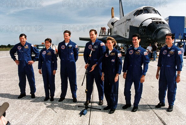 With the Space Shuttle Orbiter Columbia in the background, STS-83 Mission Commander James D. Halsell (center) gives a post-landing briefing on Runway 33 at KSC’s Shuttle Landing Facility ca. 1997