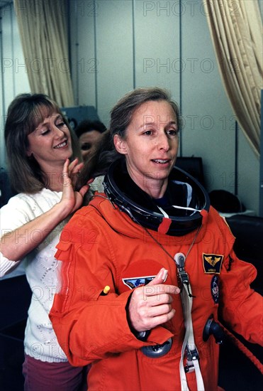 STS-81 Mission Specialist Marsha S. Ivins gets a helping hand from a suit technician as she prepares to don the helmet of her launch/entry suit in the suitup room of the Operations and Checkout (O&C) Building ca. 1997