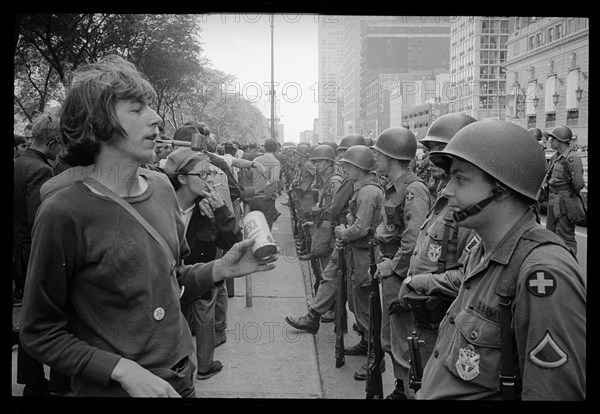 Young hippie standing in front of National Guard soldiers