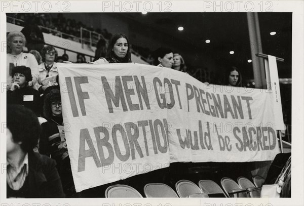 Photograph of women attendees holding a banner reading, "If Men Got Pregnant Abortion Would Be Sacred" at the National Women's Conference, Houston, TX, 11/1977.