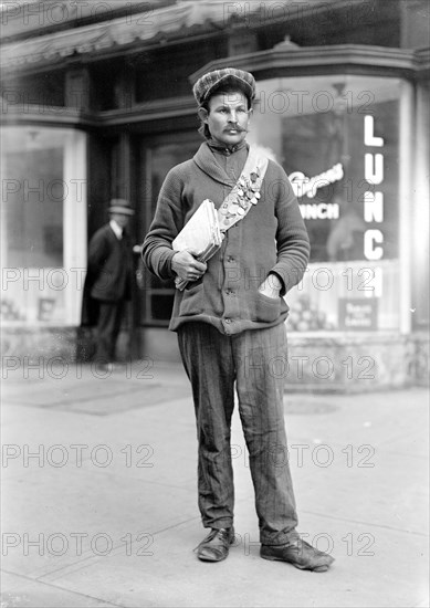 Early 1900s man in American city holding books or papers and wearing a medal covered sash