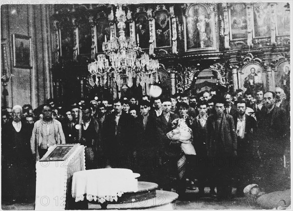 Serbian civilians who are being forced to convert to Catholicism by the Ustasa regime stand in front of a baptismal font in a church in Glina. 30 July 1941