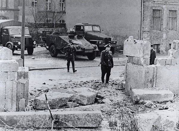 The refugees rammed the wall with a heavy truck and then fled on foot into the French Sector of West Berlin when their truck stalled in the rubble. The East German guards fired several shots at them but missed. In the background are Communist military vehicles posted after the incident to prevent further escapes.