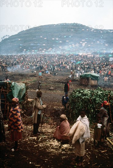1994 - A group of refugees with the refugee camp in the background.