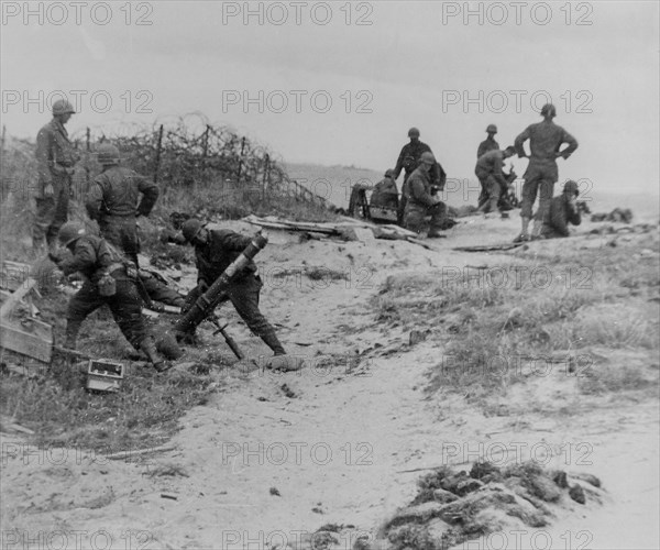 A mortar crew stands back just before firing into a Nazi position somewhere along the Normandy Coast, France.