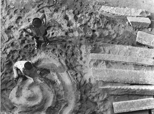 deux enfants jouent avec des balles sur une piste de sable, 1962