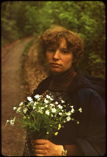Young caucasian woman with a bouquet of daisies on a background of the road, turning to the forest.