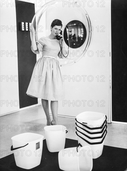 A woman on the phone with plastic buckets stacked, 1960