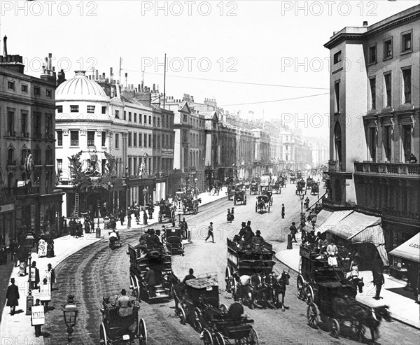 Regent Street with horses and carriages and lots of people in the street.