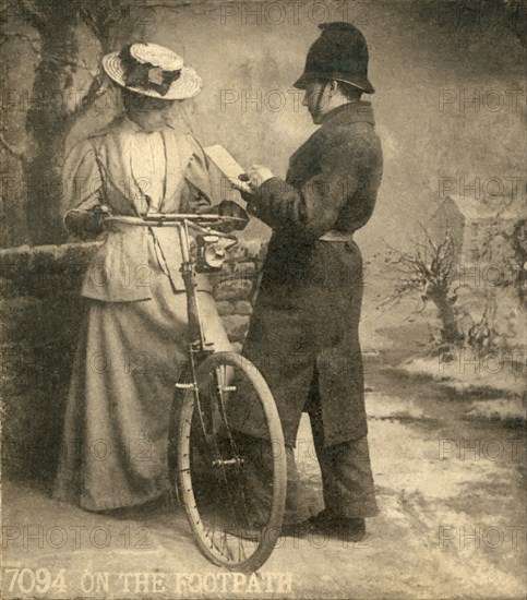 On the footpath, a policeman writing a ticket for a lady riding her bike on the footpath.