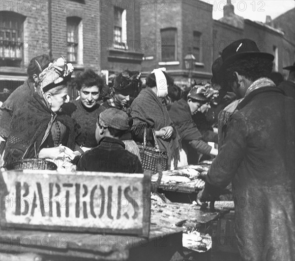 A fishmonger stall in the market with lots of people buying fish.