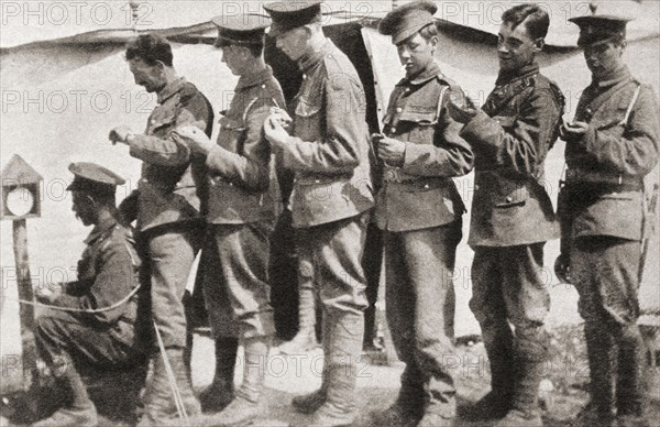 Soldiers during World War One sychronising their watches with a clock mounted on a post in the camp.