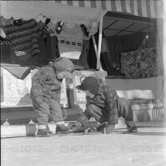 Steering; boy helping girl to put on her skis; 1957