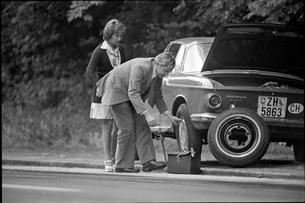 Man helps female driver with flat tire, 1974