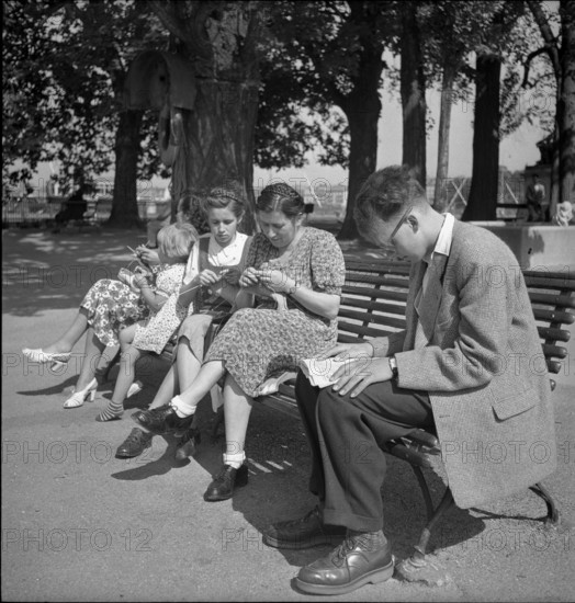 Genf: Ile Rousseau, man reading newspaper, women knitting; 1949.