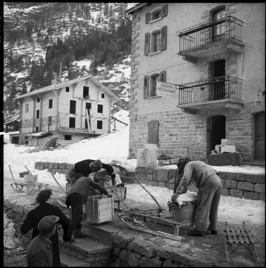 Herbriggen, village threatened with landslide, evacuation, men loading goods on sledge; 1959.