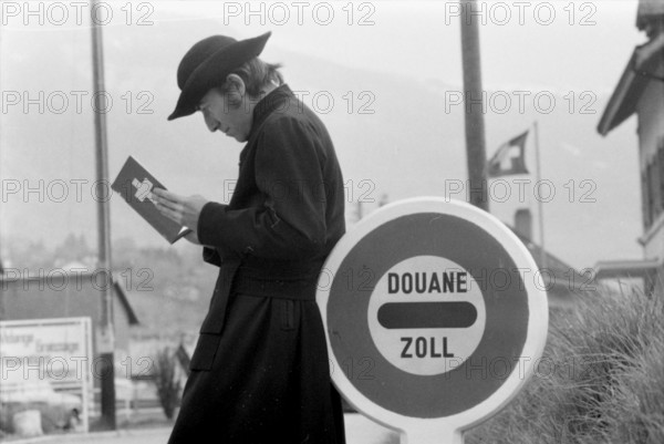 Jesuit leaning on customs sign, 1973.