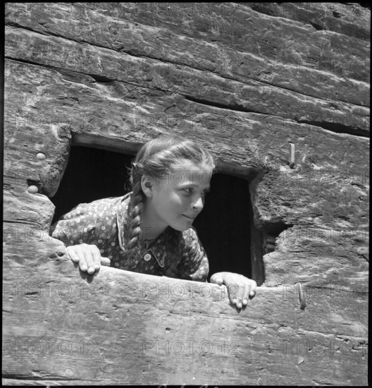 Girl looking out of the window of a baking house in the Valais, 1941.