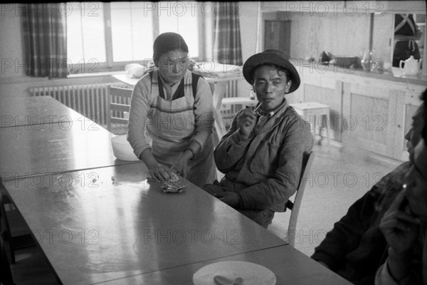 Tibetan woman cleaning table, man smoking, Waldstatt 1962.