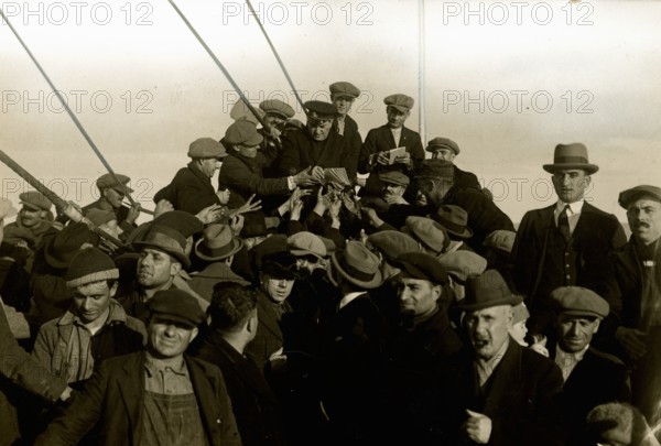 Group of emigrants around the chaplain on the foredeck of the Conte Verde