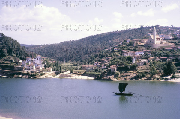 A series of images about port wine production in Portugal c 1960 - traditional rabelo boat sailing boat passing River Douro village.