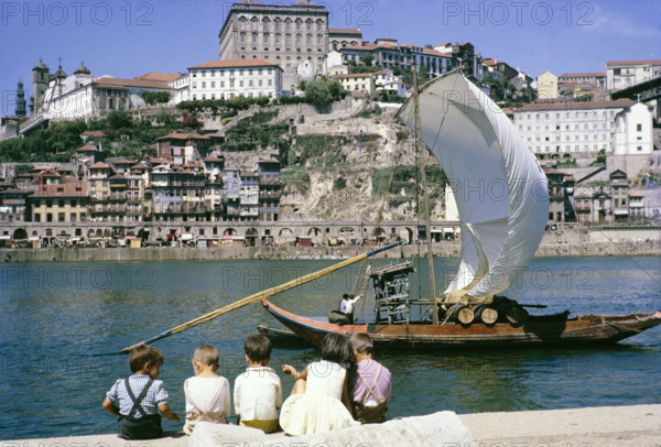 A series of images about port wine production in Portugal c 1960 - traditional rabelo boat with oak barrels in city of Porto, children sitting on quayside.