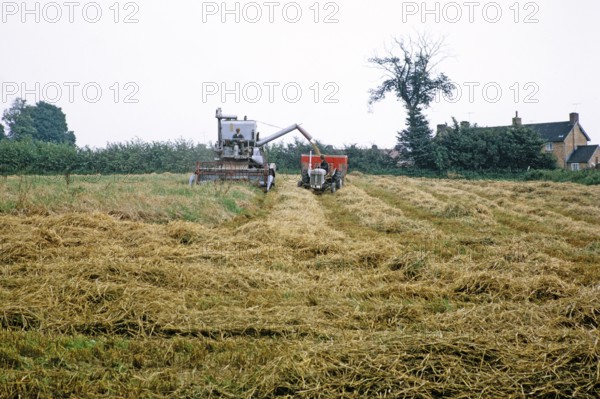 Claas combine harvester harvesting in field with tractor and trailer, England, UK 1968.