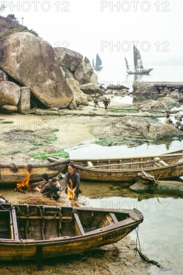 Cleaning the hull of a boat with flames from a small fire in a process known as breaming, Castle Peak, New Territories, Hong Kong, Asia, 1964.